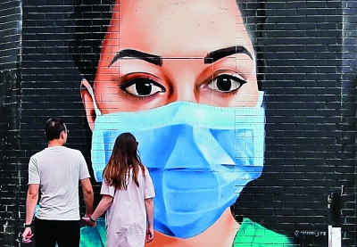 4月26日，在英国伦敦，一对情侣从一幅画有戴口罩医护人员的壁画前走过。